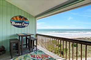 A balcony with a view of the ocean, a table with chairs, and a sign reading "Mama Caye". - Beautiful Condo With Amazing Ocean Views (Surf City)
