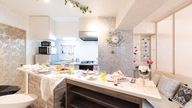 Une cuisine moderne avec des meubles blancs, un coin repas avec une table dressée, et un mur décoratif orné d’un motif en mosaïque.