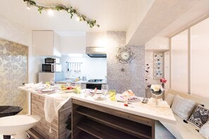 A modern kitchen with white cabinets, a dining area with a table set for a meal, and a decorative wall with a mosaic pattern. - Papillon Paradis Higashi-Shinjuku (Tokyo)