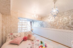Ein Schlafzimmer mit blumigem Bettbezug, einer Kristallleuchtre und Wandtapete mit Muster.
