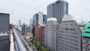 Un paysage urbain avec des immeubles modernes de grande hauteur, un pont piétonnier et une rue animée, où l’on voit des véhicules et de la verdure.