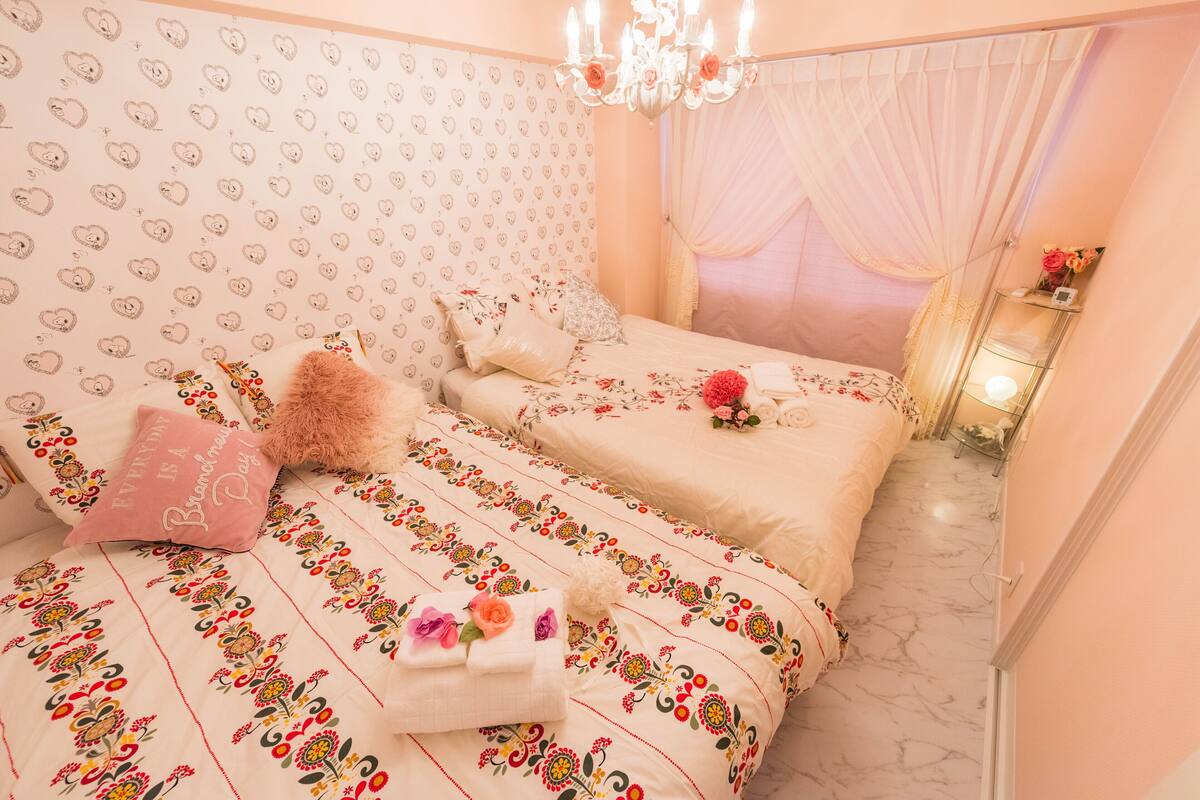 Une chambre avec deux lits, une literie à motifs floraux, un lustre et une table de chevet avec une lampe.