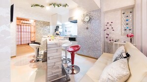Un salon moderne comprenant un canapé, deux tabourets de bar, un coin cuisine et un mur décoratif.