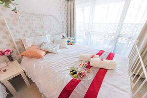 A neatly made bed with a white headboard, a red and white striped runner, and a bouquet of flowers on the bed.