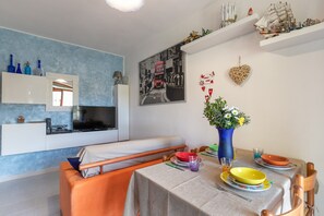 Et moderne værelse med en seng, et spisebord dækket med tallerkener og en vase, et fjernsyn og en reol med pynteting.