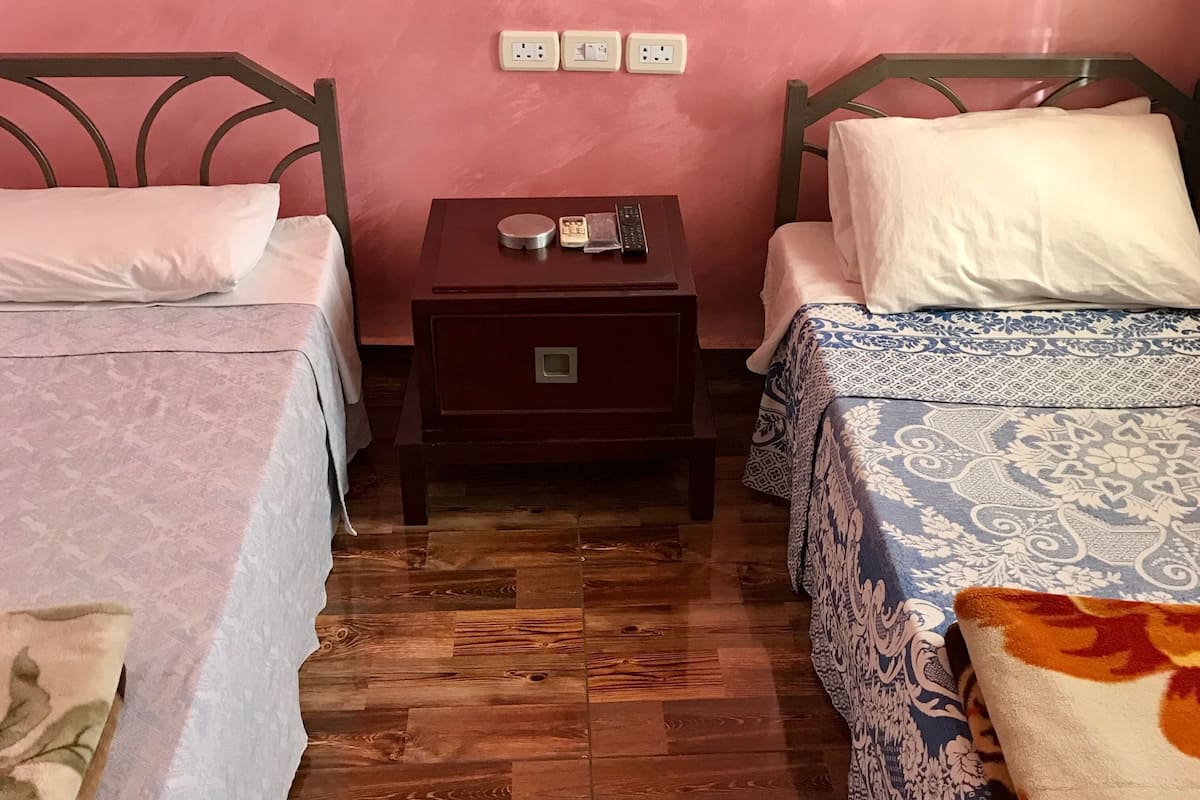 A room with two beds, a small wooden nightstand, and a wall socket.