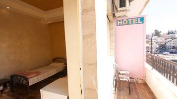 A hotel room with a single bed, a small table, and a balcony with a chair.