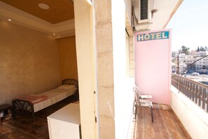 Ein Hotelzimmer mit einem Einzelbett, einem kleinen Tisch und einem Balkon mit einem Stuhl.