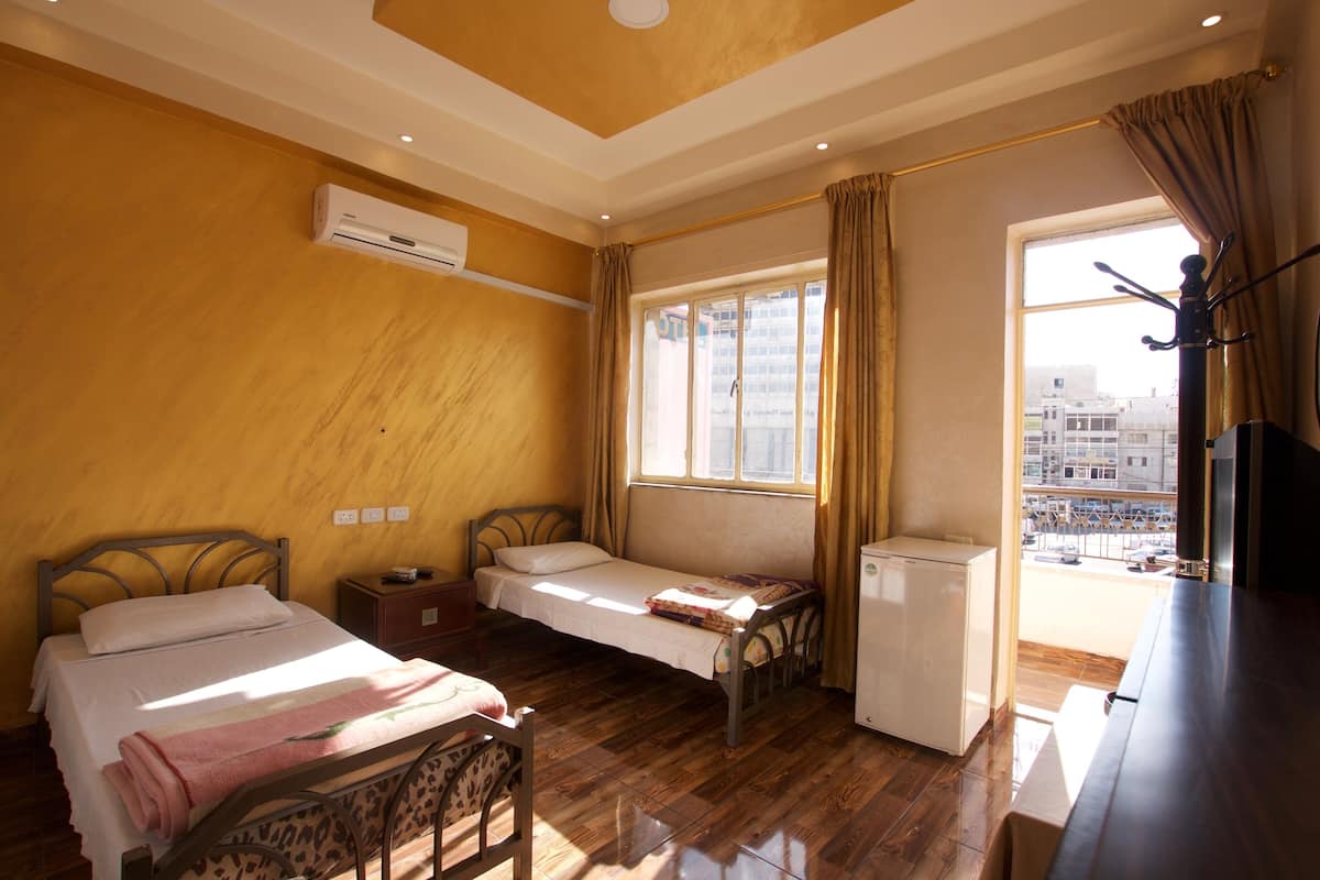 A room with two beds, a small refrigerator, and a window with curtains.