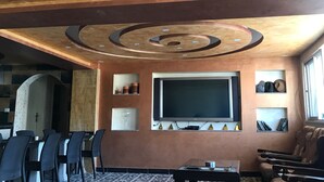 A room with a large flat-screen TV, a seating area with chairs, a coffee table, and a decorative ceiling with circular patterns.
