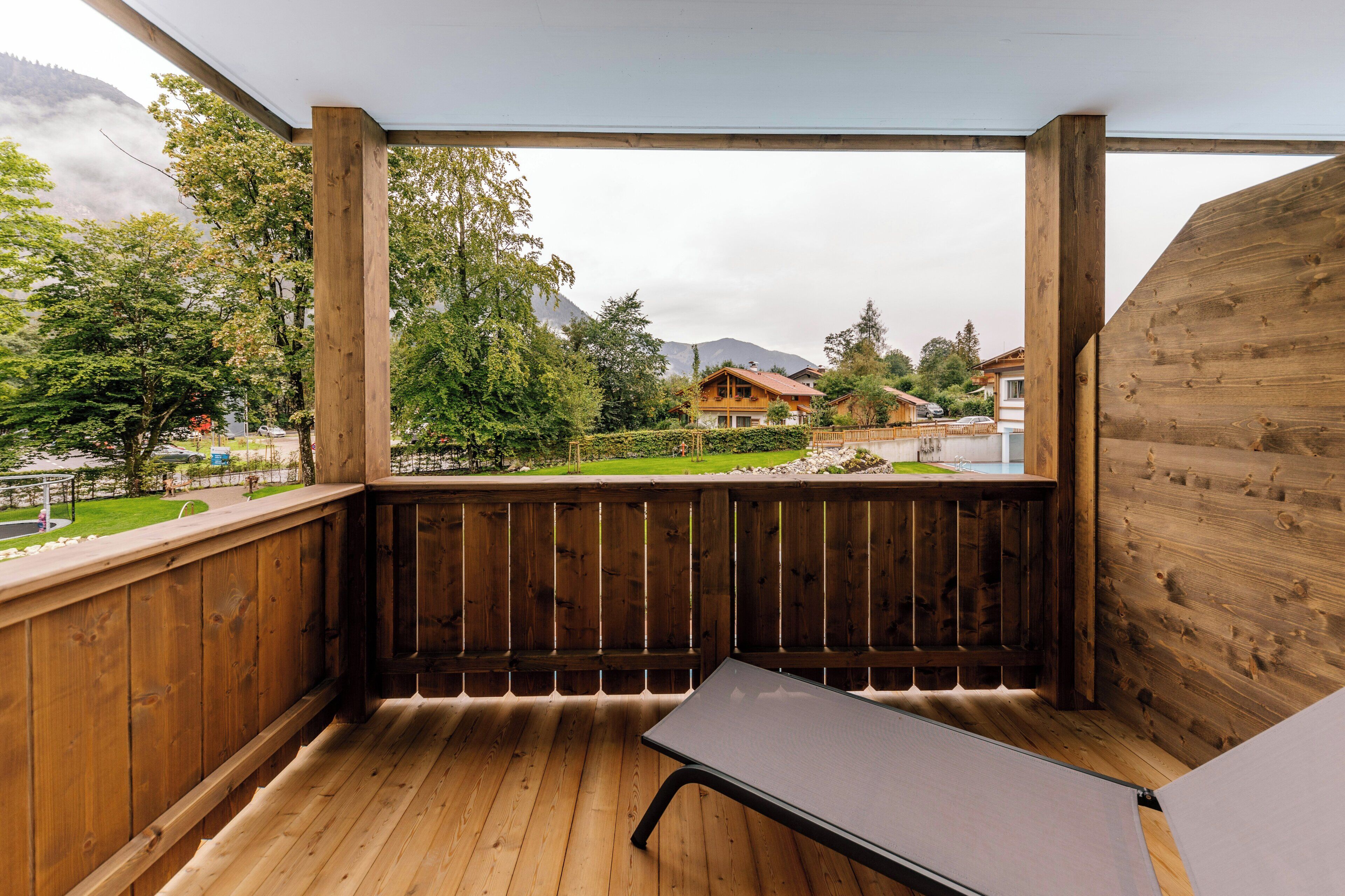 Ein Holzbalkon mit Tisch und Stühlen, der auf eine grüne Landschaft mit Bäumen und Häusern blickt.