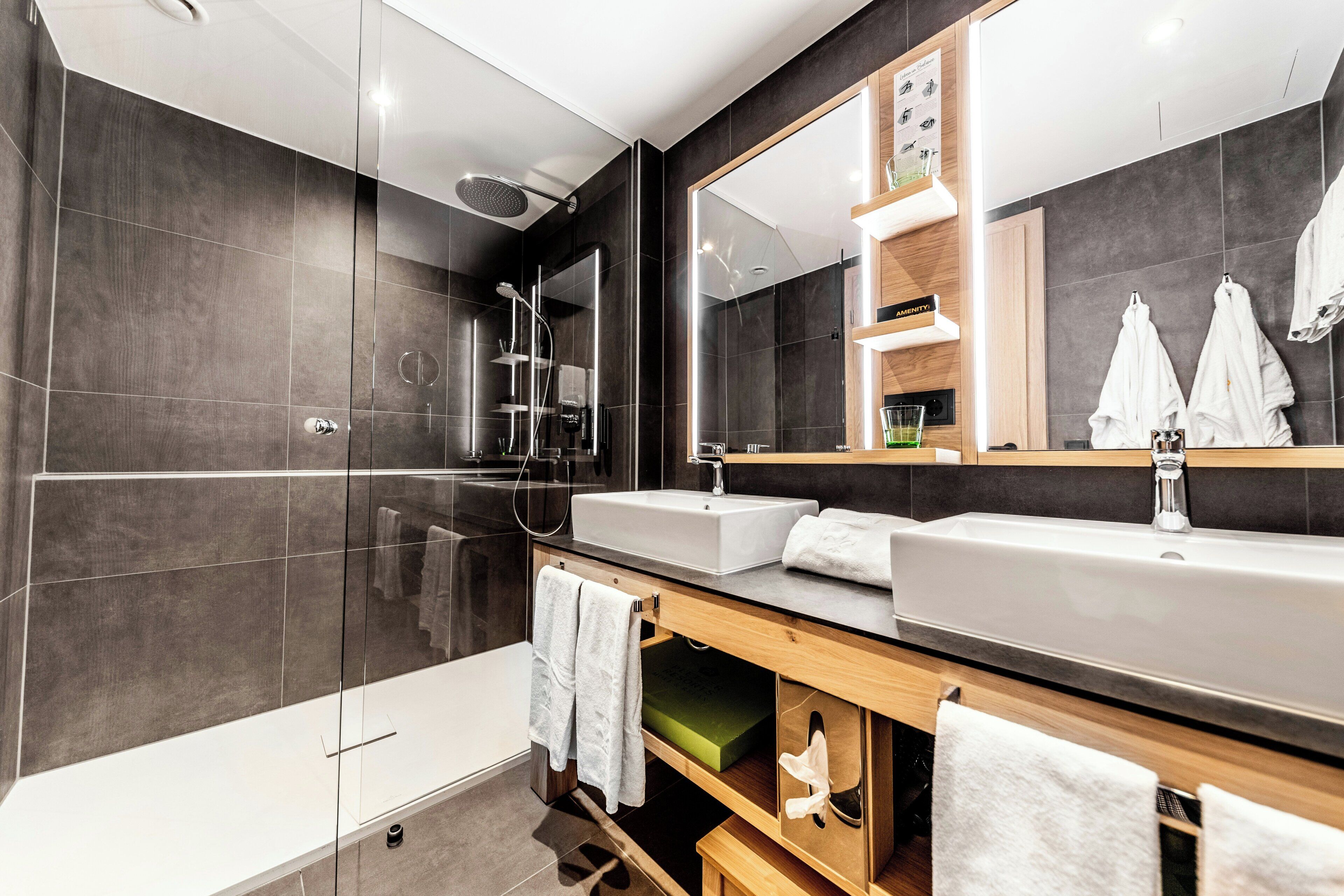Un baño moderno con ducha envuelta en vidrio, un espejo grande y un tocador con lavamanos y perchero.
