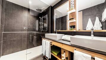 Un baño moderno con ducha envuelta en vidrio, un espejo grande y un tocador con lavamanos y perchero.