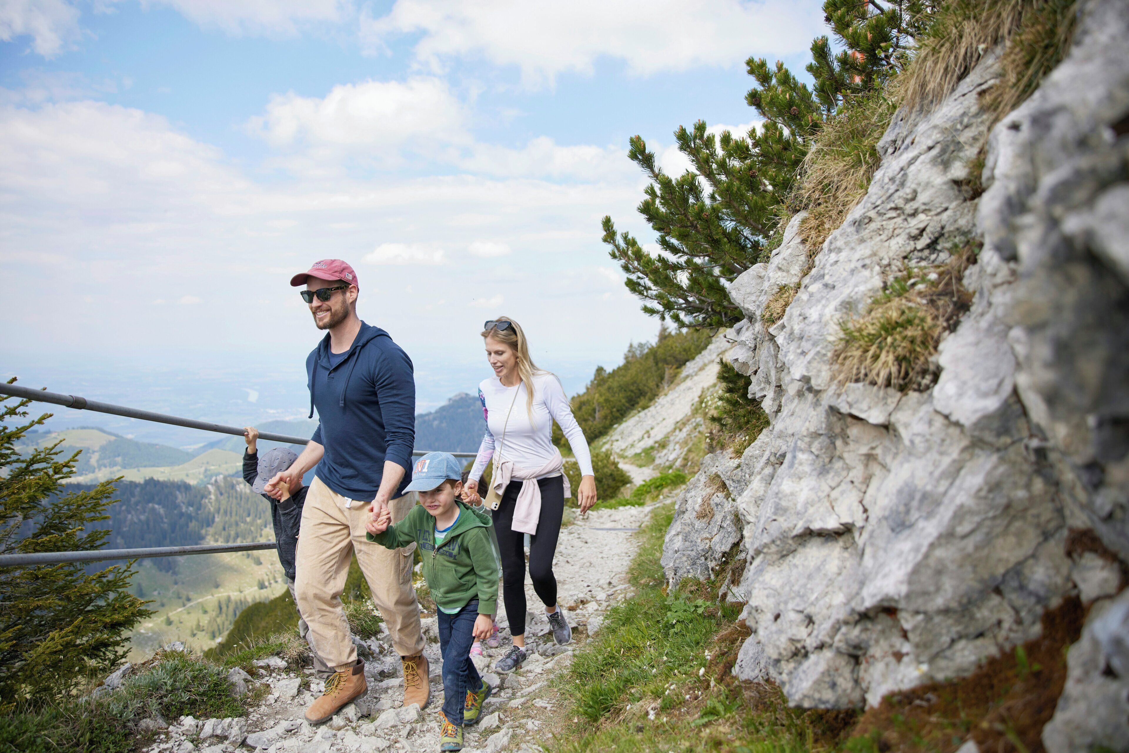 A family hiking on a rocky trail with a mountainous landscape in the background.