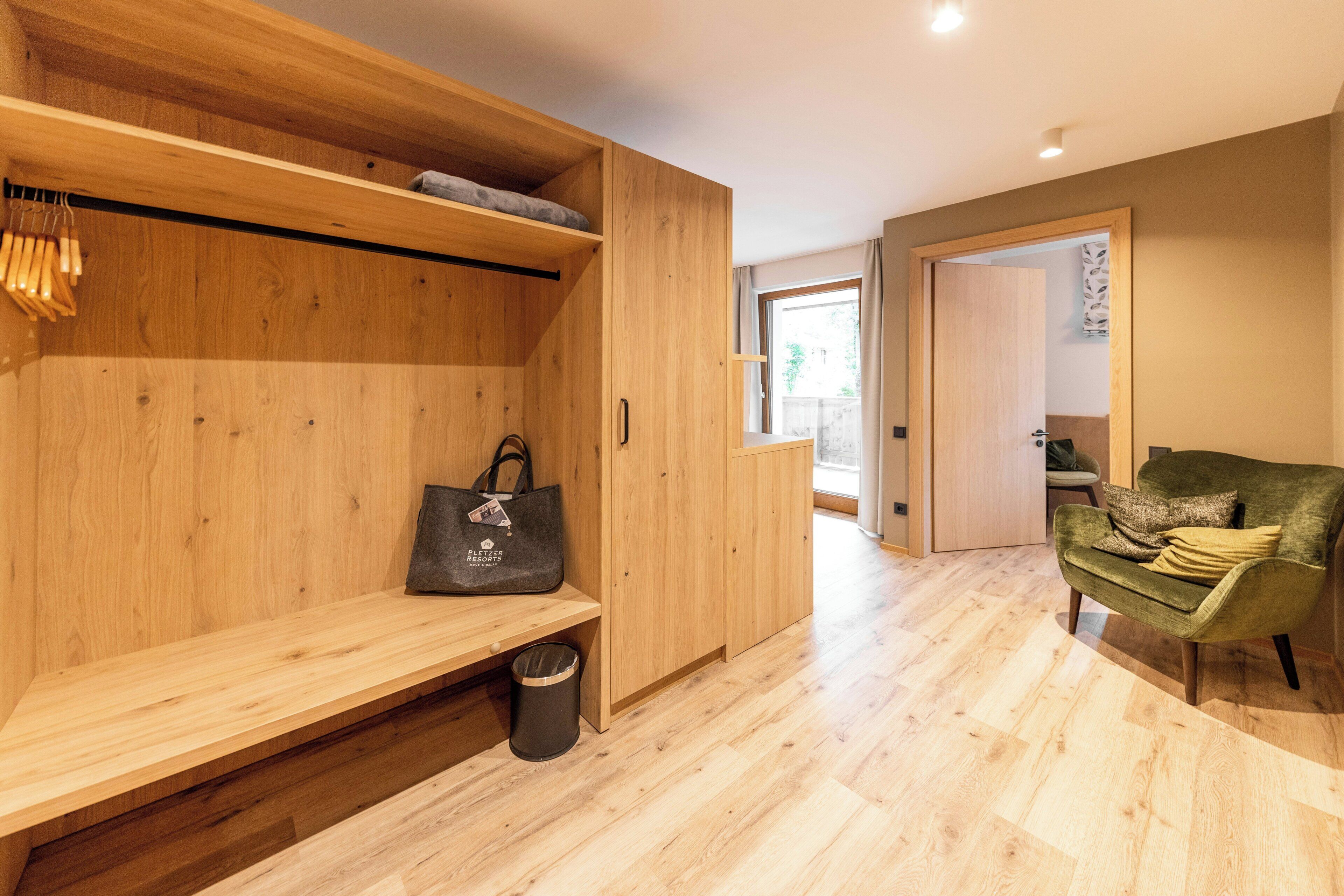 Um interior moderno com um banco de madeira, uma poltrona verde e um guarda-roupa com uma bolsa pendurada.