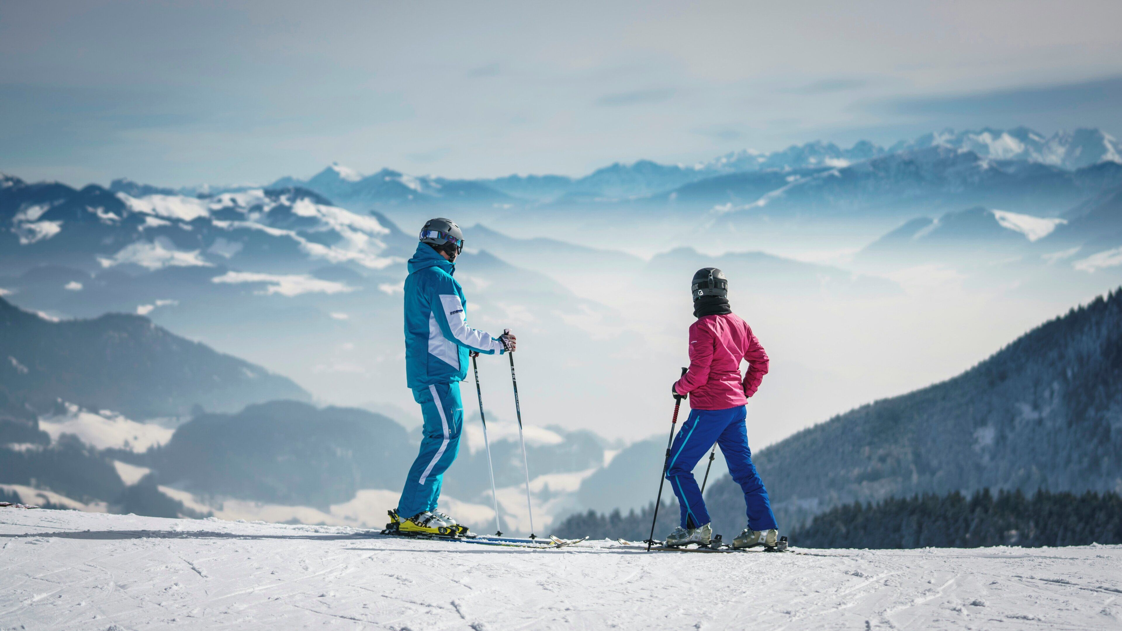 Two skiers on a snowy mountain slope with a view of distant mountains.