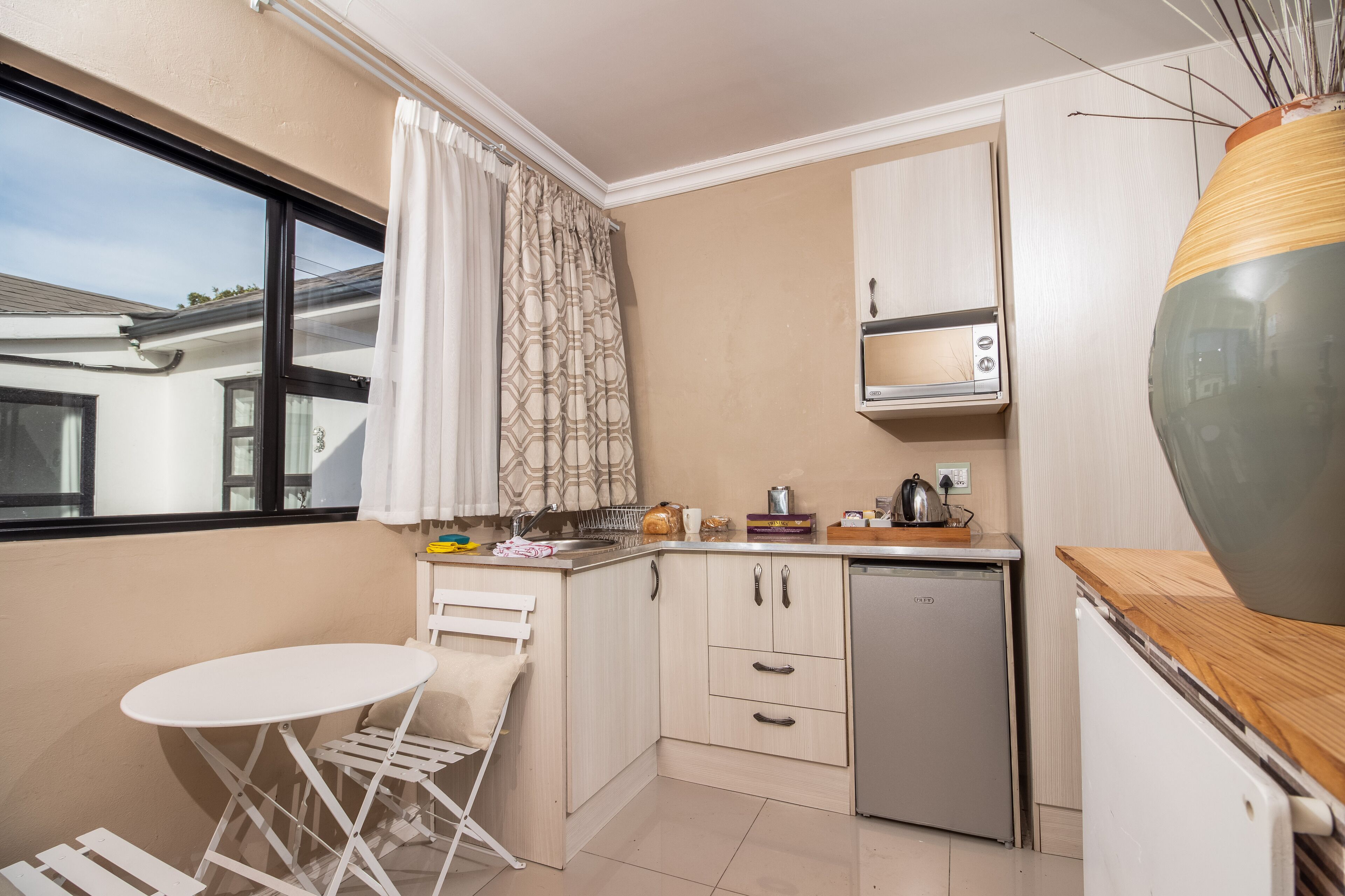 A compact kitchen with a small dining table, a dishwasher, and a window with curtains.