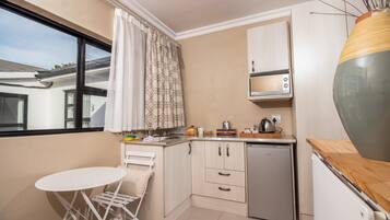 A compact kitchen with a small dining table, a dishwasher, and a window with curtains.