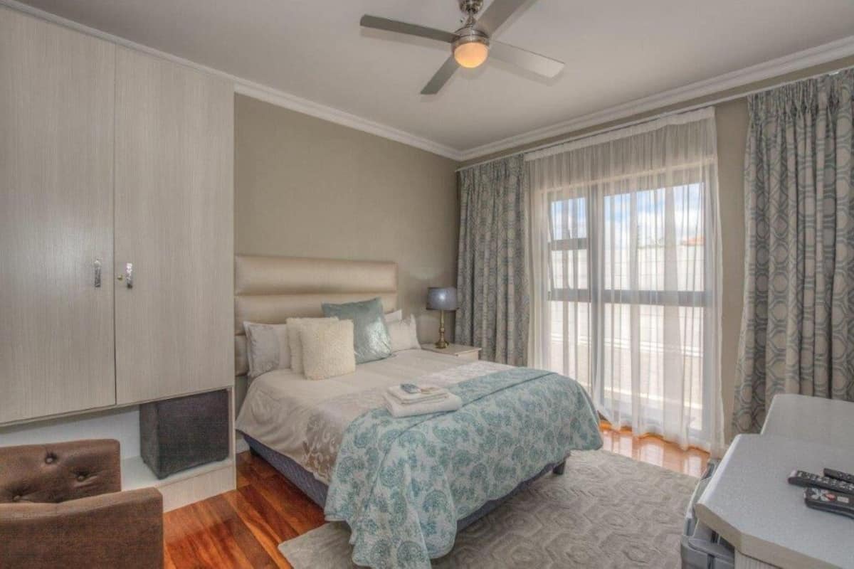 A bedroom with a bed, a ceiling fan, a nightstand, a chair, a table, and curtains.