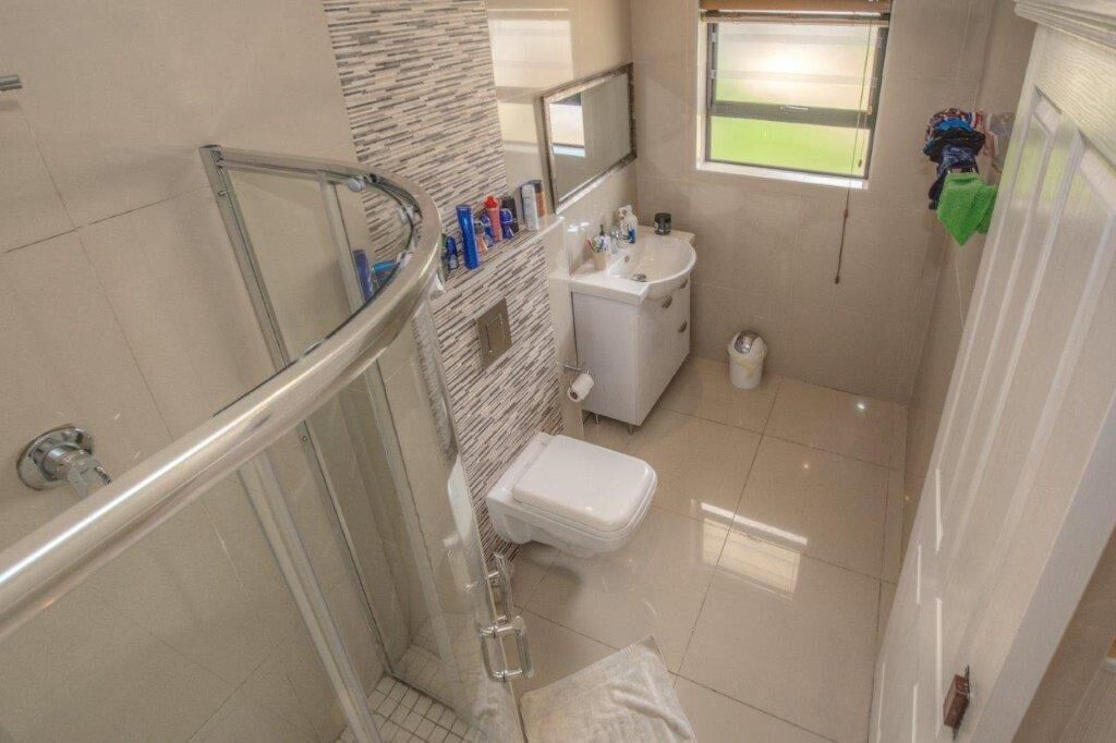 A bathroom with a glass shower enclosure, a toilet, a sink, and a window.