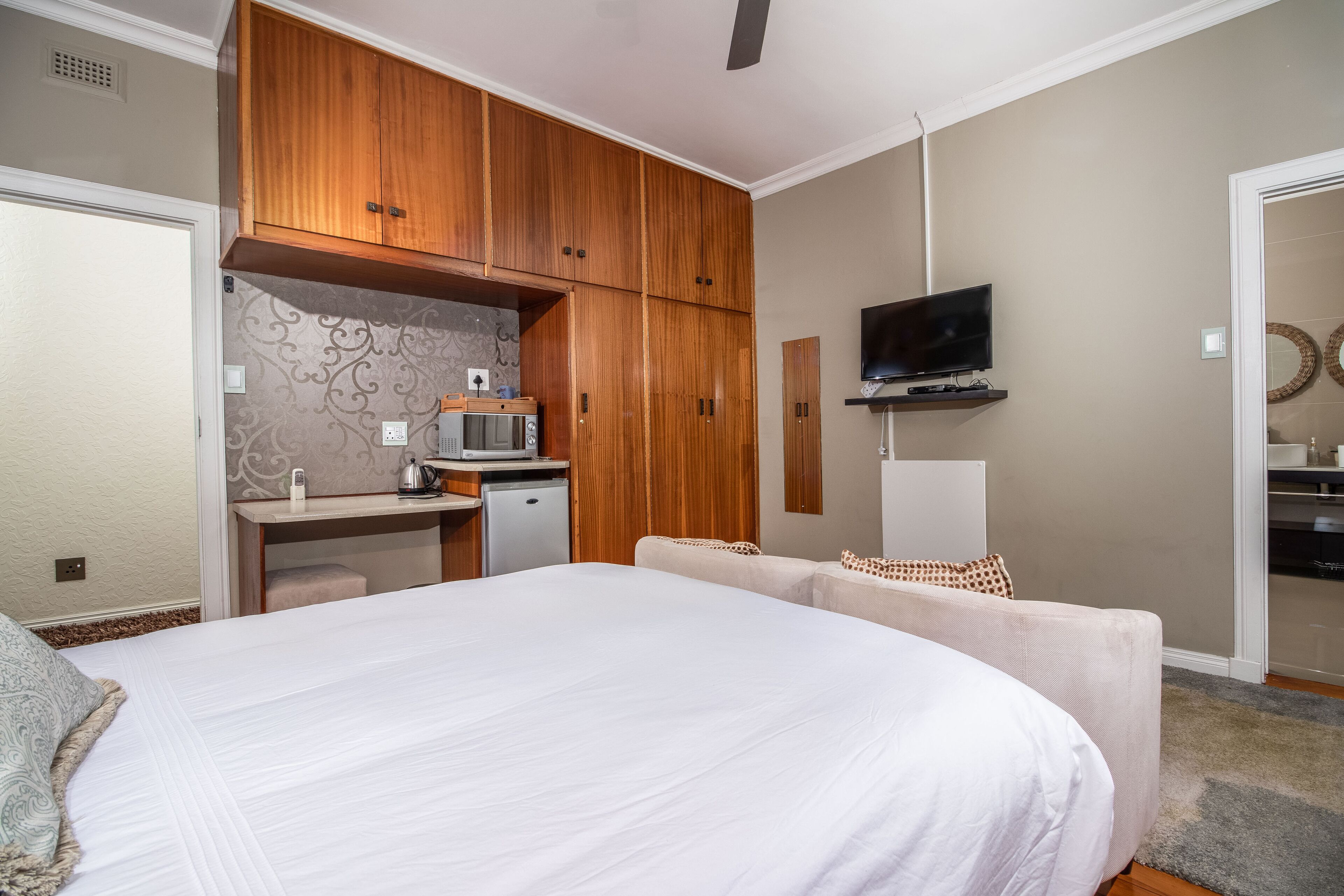 A bedroom with a large bed, a desk with a microwave, a TV, and a wardrobe.