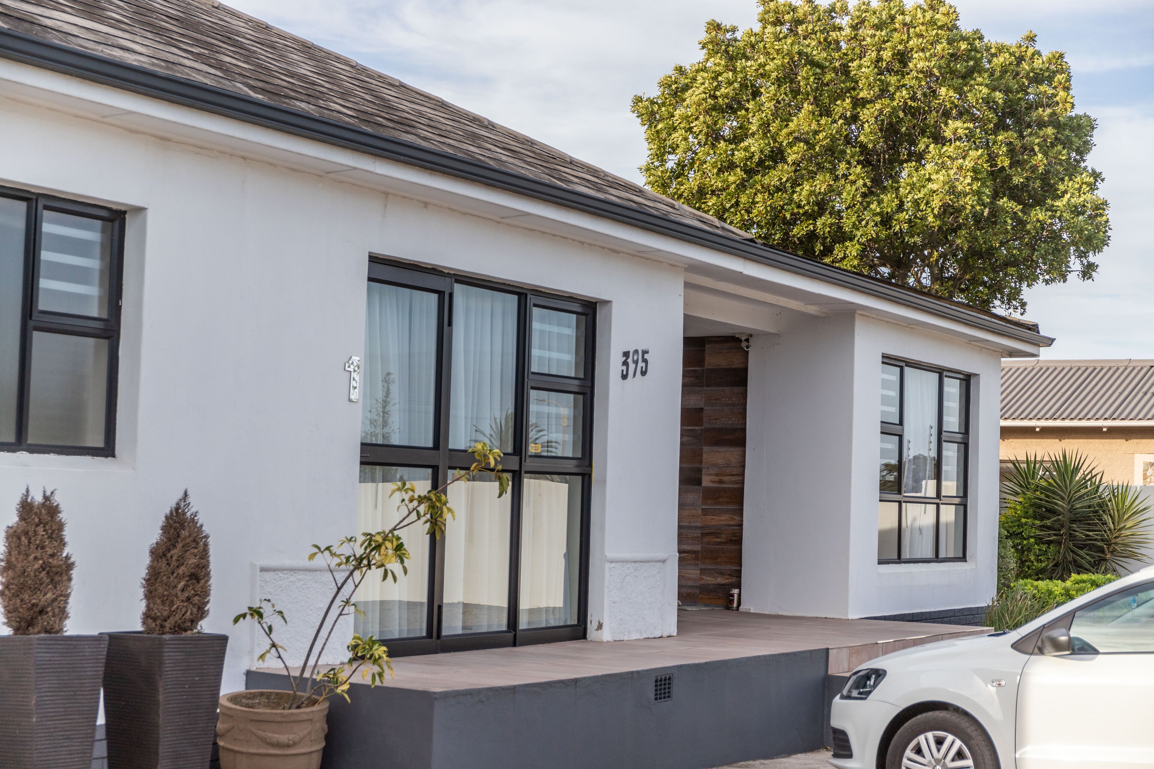 Une maison moderne à deux étages, dotée de grandes fenêtres, portant le numéro 395, et devant laquelle est garée une voiture.