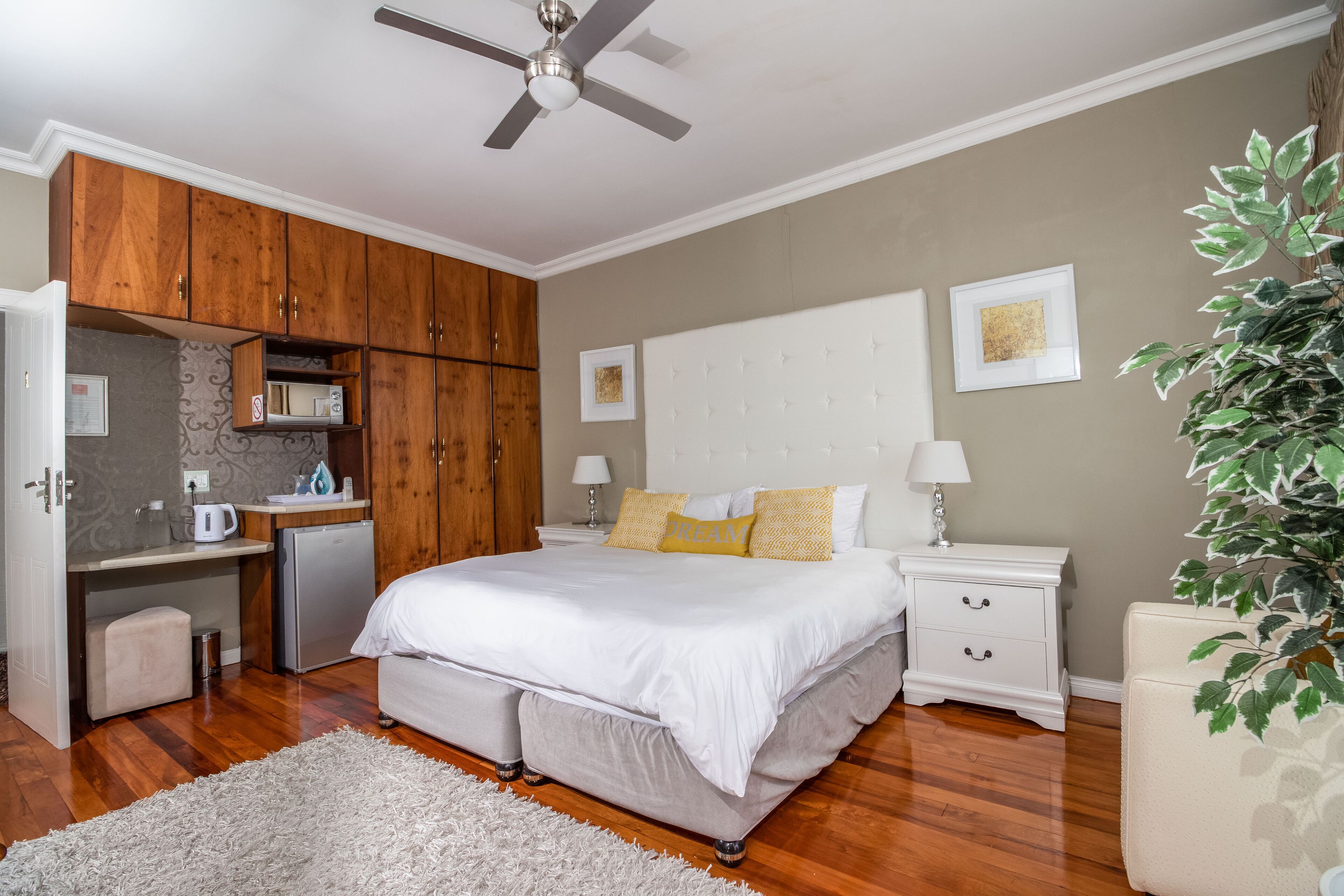 Un dormitorio con cama, mesitas de noche, escritorio, ventilador de techo y una planta en maceta.