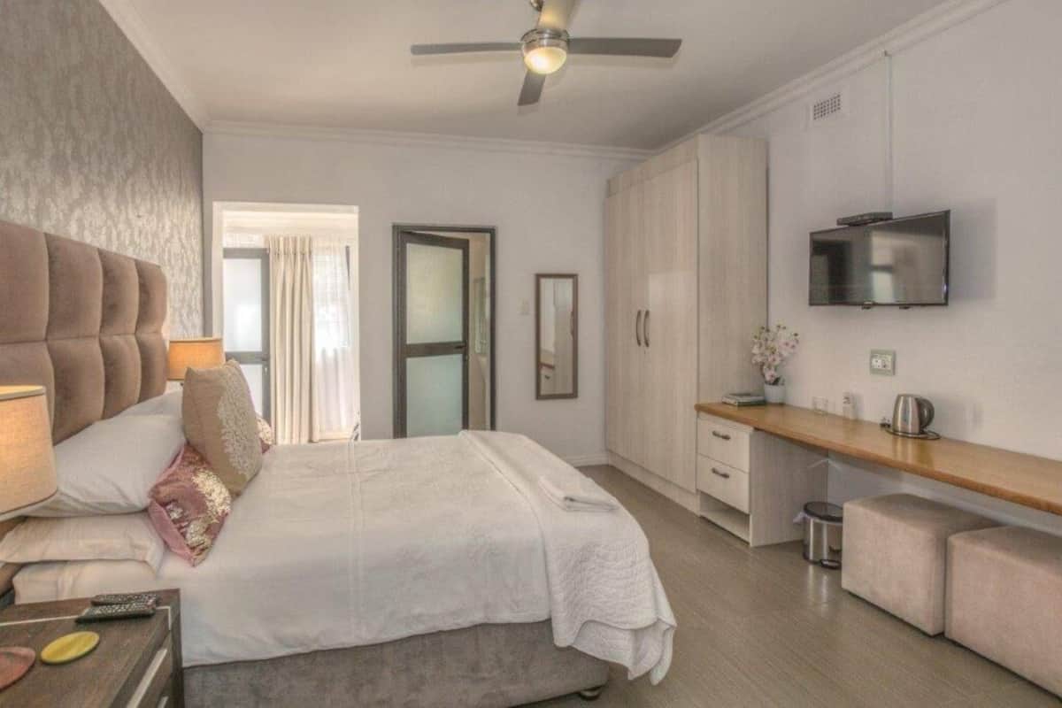 A modern hotel room with a bed, a desk, a TV, and a ceiling fan.