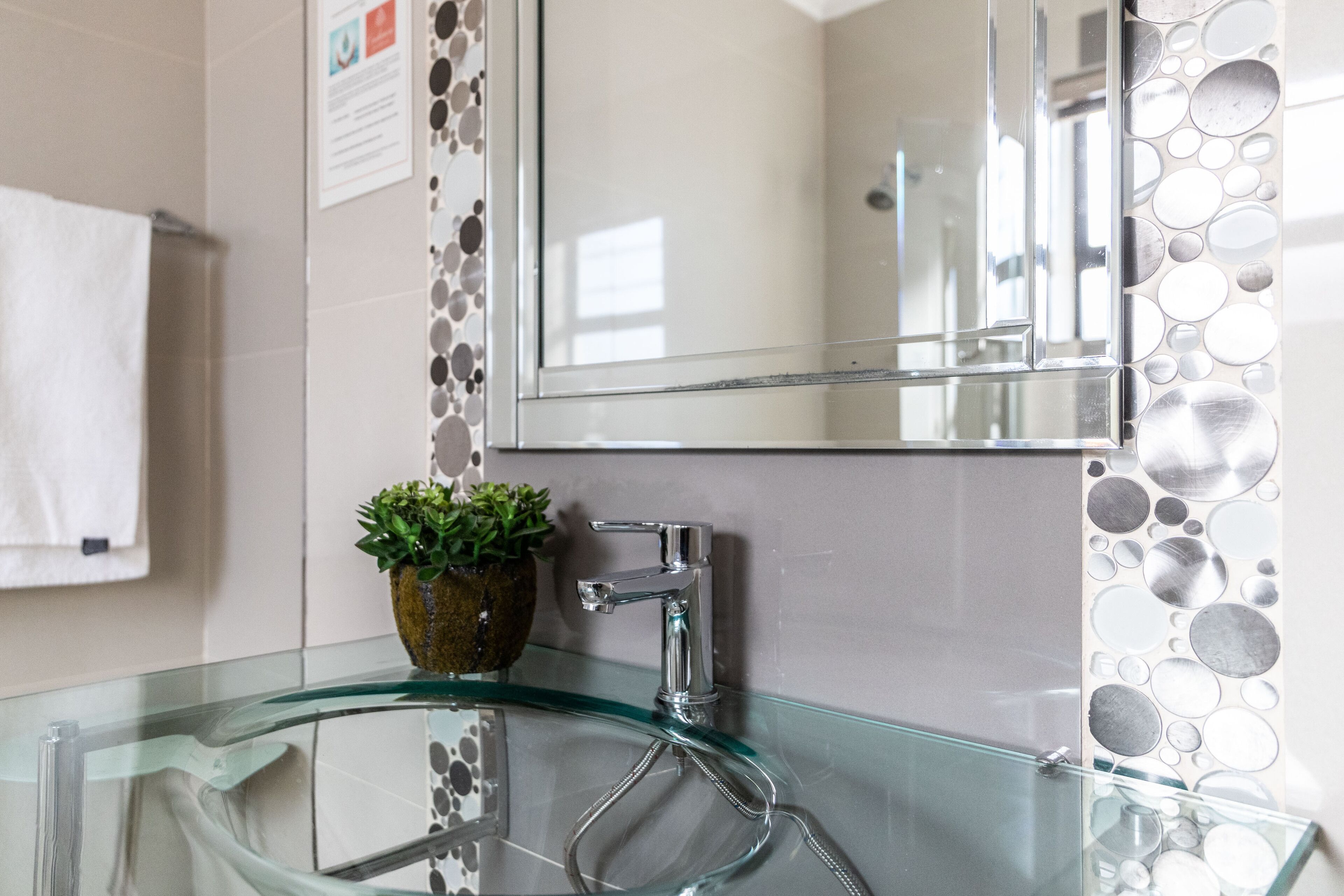 A modern bathroom with a glass sink, a potted plant, and a mirror with a decorative wall panel.