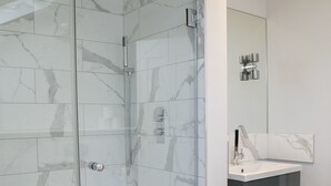 Un baño moderno con ducha envuelta en vidrio, una bañera blanca y un tocador con espejo.