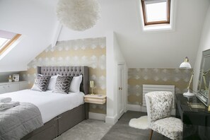 A bedroom with a bed, bedside table, lamp, chair, and a small window.