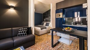 Een ruimtelijk ingerichte leefruimte met kitchenette, een bank, een eettafel en een bed.