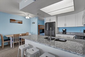 A compact kitchen with a granite countertop, white cabinets, a stainless steel refrigerator, and a coffee maker.