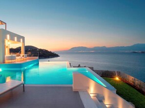 Una piscina infinita moderna con vistas al mar y montañas distantes.