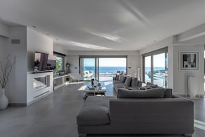 Ett modernt vardagsrum med en stor grå soffa, en matplats och utsikt över havet.