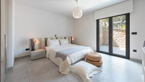 A modern bedroom with a large bed, bedside lamps, a hanging light fixture, and a view through a sliding glass door. - Welcome to Villa Soligia! Beach Front Villa Large Private Pool Amazing Sea View (Corinth)