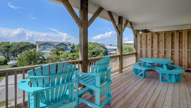 A wooden deck with turquoise Adirondack chairs and picnic tables, overlooking a residential area with houses and trees. - Island Oasis, Elevator, Beautiful Decor (Topsail Beach)