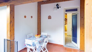 Un patio cubierto con una mesa lista para dos personas, una cesta de fruta y una puerta que da a un espacio interior.
