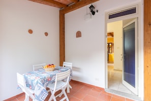 Zona pranzo con tavolo apparecchiato per due, un cesto di frutta e un lampadario a parete.
