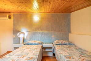 Una camera da letto con due letti, un comodino con una lampada, un termosifone a parete e una piccola finestra.