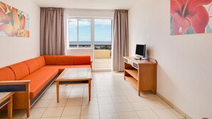 A living room with a sofa, a coffee table, a TV on a wooden stand, and a balcony with a view. - Apartments Palm Garden (Pajara)