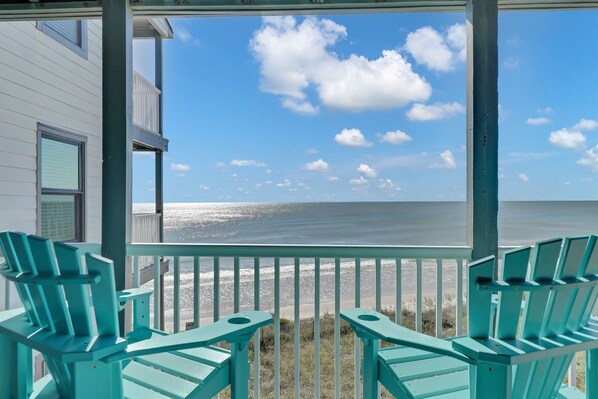A porch with two chairs facing a beach view.