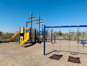 A playground with a yellow slide, swings, and a climbing structure. - Oceanfront Condo with amazing views of The Atlantic (North Topsail Beach)