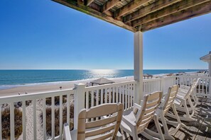 A beachside patio with white chairs and a wooden pergola overlooking the ocean.