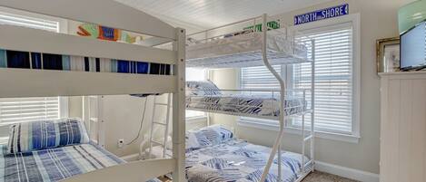 A bunk bed room with a North Shore sign, a window with blinds, and a television on a cabinet.