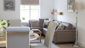 A living room with a sofa, armchair, and coffee table. There is a window with blinds, a lamp, and a picture frame on the wall.