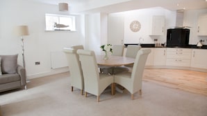 A modern kitchen with white cabinets, a black refrigerator, and a wooden dining table with six chairs.