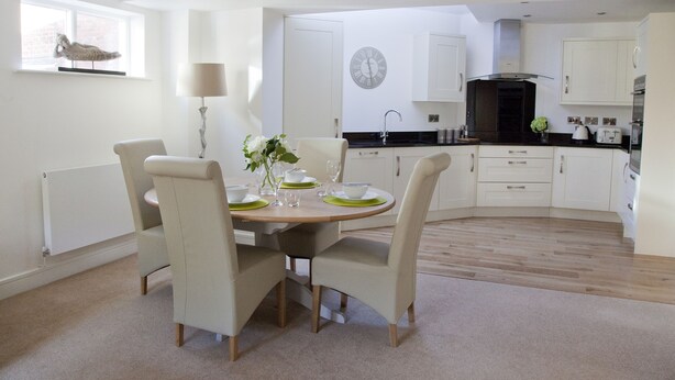 A modern kitchen with white cabinetry, a round dining table with chairs, and a clock on the wall.