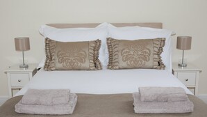 A neatly made bed with two pillows, two folded towels, and two bedside lamps on white nightstands.
