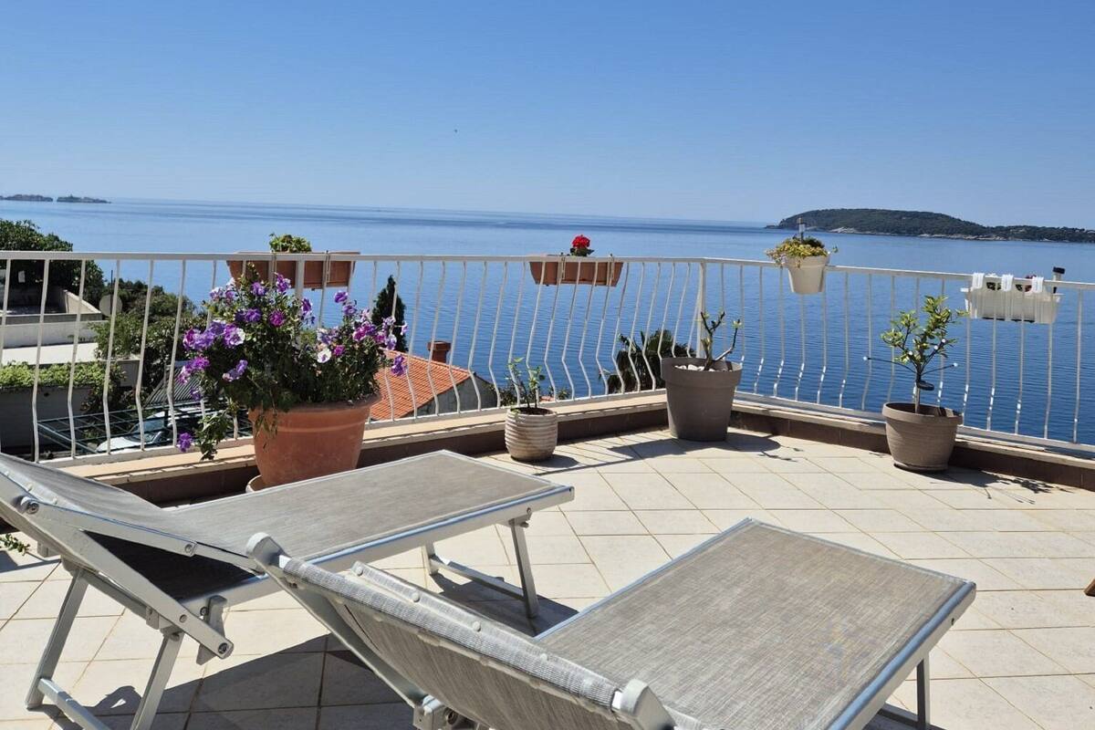 Una terraza con dos tumbonas, plantas en macetas y vistas al mar.